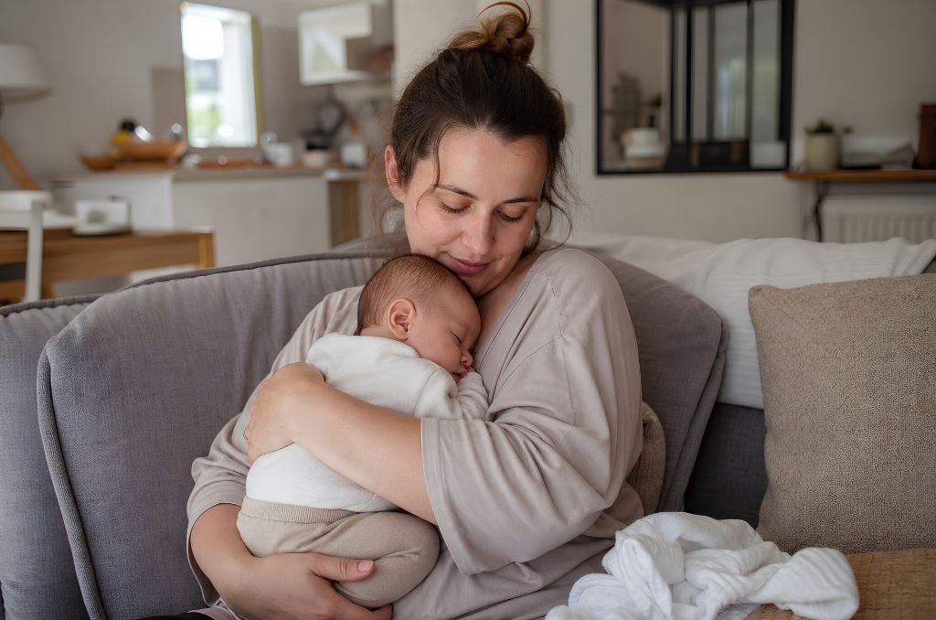 Maman tenant tendrement son nouveau-né emmailloté contre elle sur un canapé