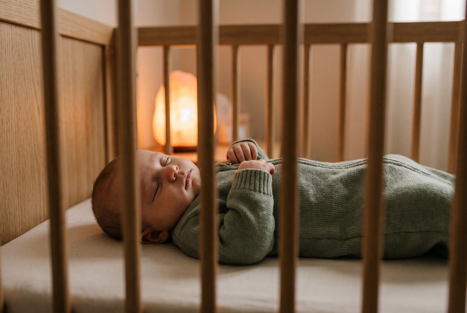 Bébé endormi sur le dos dans son lit à barreaux, veilleuse à lumière chaude allumée