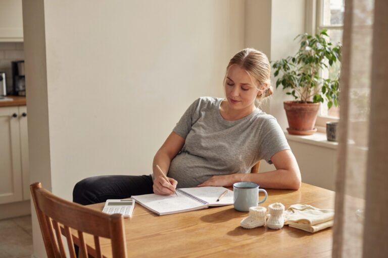 Future maman calculant le budget de sa liste de naissance à la table de la cuisine