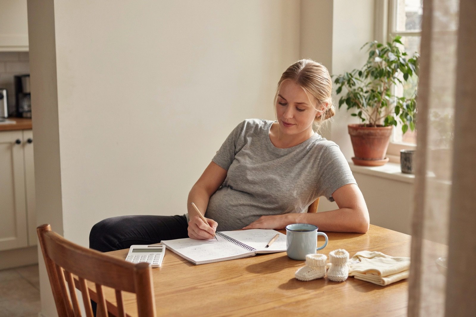 Future maman calculant le budget de sa liste de naissance à la table de la cuisine
