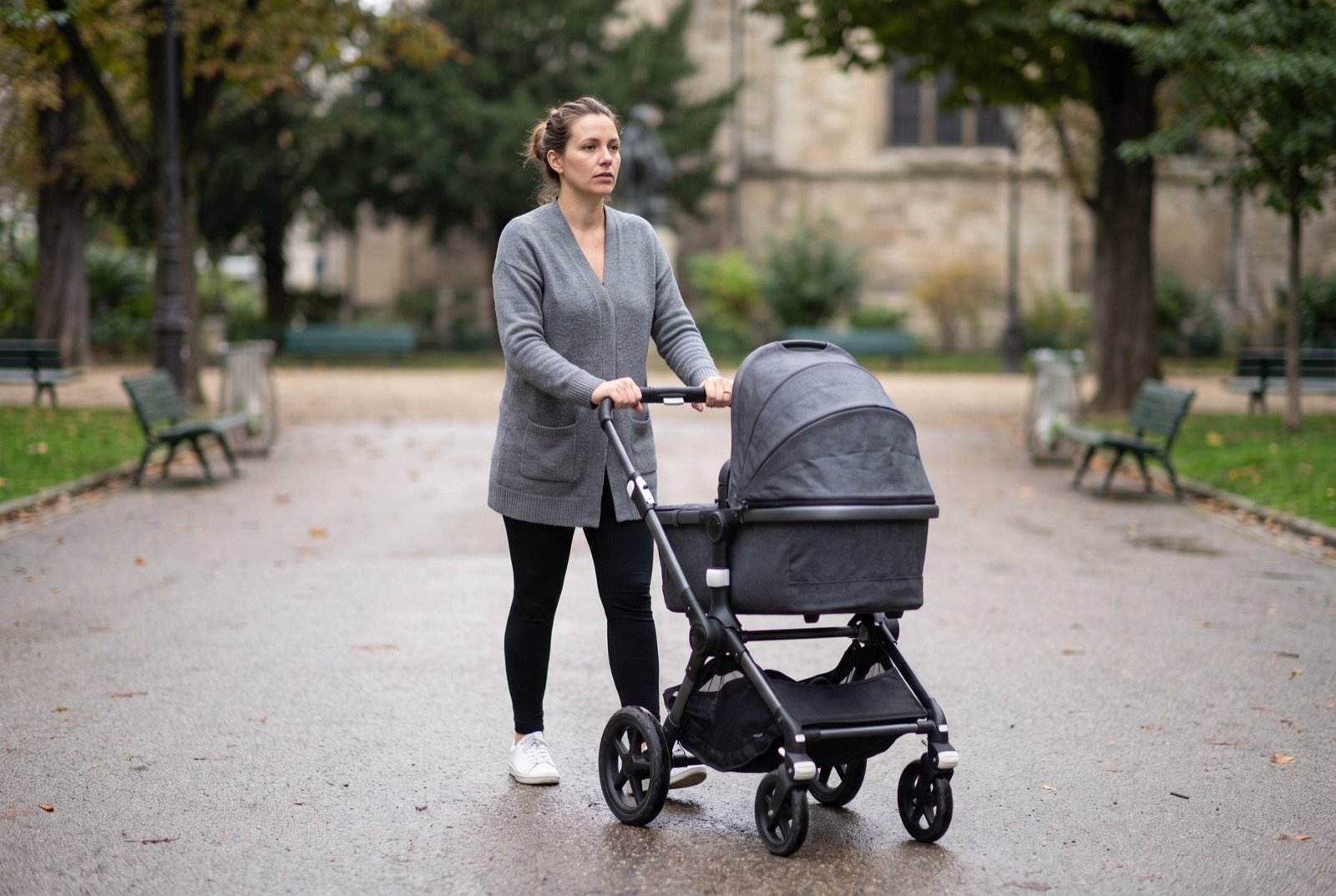 Jeune maman qui marche doucement dans un parc en poussant le landau de son bébé