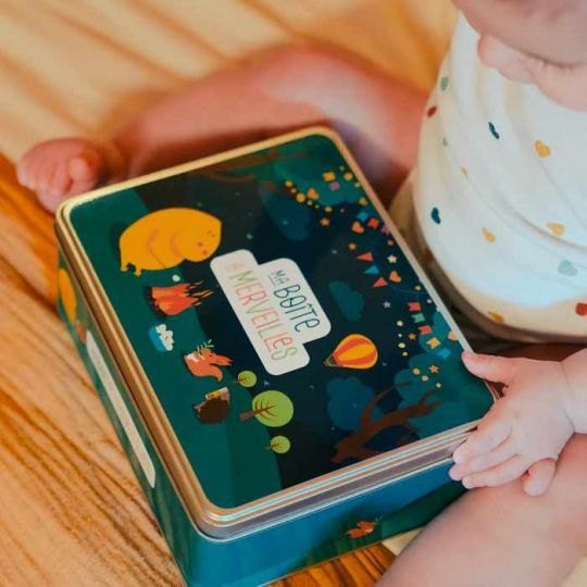 Bébé assis près de la boîte en métal du coffret Merveilles Pototam Bébé assis près de la boîte en métal du coffret Merveilles Pototam