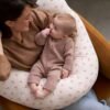 Coussin d'allaitement Cherry Vertbaudet porté Maman dans un fauteuil avec son bébé installé sur le coussin d'allaitement Cherry Vertbaudet