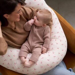 Coussin d'allaitement Cherry Vertbaudet porté Maman dans un fauteuil avec son bébé installé sur le coussin d'allaitement Cherry Vertbaudet