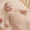 gigoteuse-velours-beige Bébé souriant allongé sur le dos dans un lit à barreaux, en gigoteuse à manches en velours côtelé beige Vertbaudet