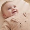 Bébé allongé en gigoteuse velours côtelé Vertbaudet Bébé souriant allongé sur le dos dans son lit, en gigoteuse Vertbaudet en velours côtelé beige à oreilles de lapin