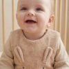 Bébé assis en gigoteuse velours côtelé Vertbaudet Bébé souriant assis dans son lit à barreaux, en gigoteuse Vertbaudet en velours côtelé beige avec oreilles et moustaches de lapin brodées