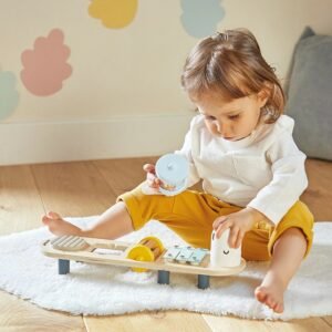 Jeune enfant assis sur un tapis, qui joue avec le stand d'éveil sonore chenille Janod en bois