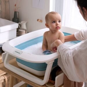 Bébé assis dans une baignoire pliante posée sur un support, accompagné d'un adulte