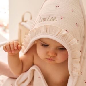 Bébé enveloppé dans une cape de bain écrue à capuche, brodée d'un prénom