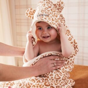 Bébé souriant enveloppé dans une cape de bain à capuche, motif léopard, tenu par un adulte